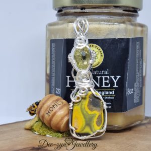 Silver filled pendant with Bumblebee Jasper and Lemon quartz stones on a wood, leaning against a jar of honey with a bee.