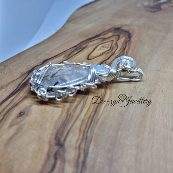 Rutilated Quartz and Rainbow Moonstone Captured in a Silver Filled Wire Sculptured Pendant on wooden background. View of left side
